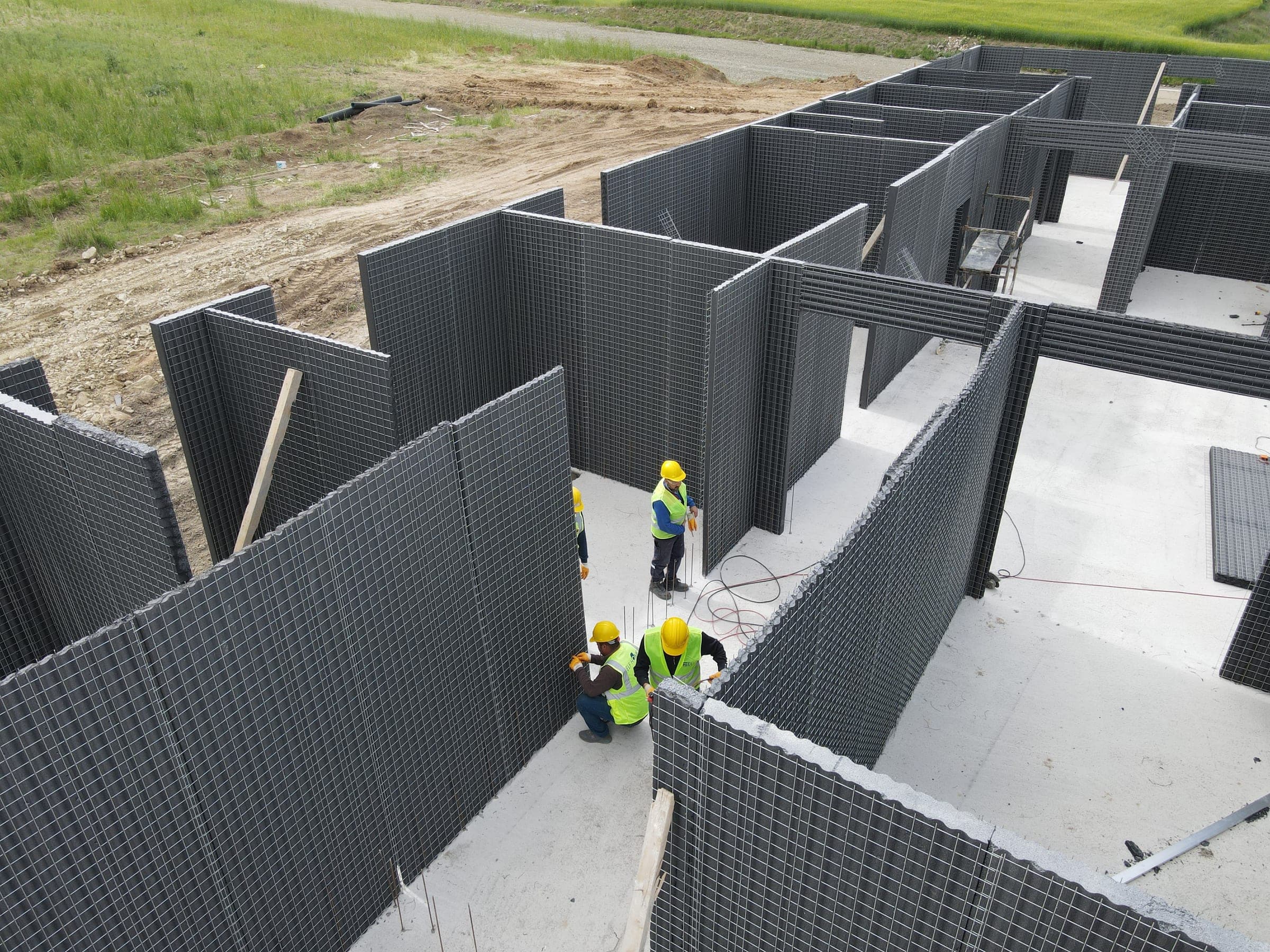 Dark EPS wall panels standing on the foundation slab while three workers in hard hats align them.