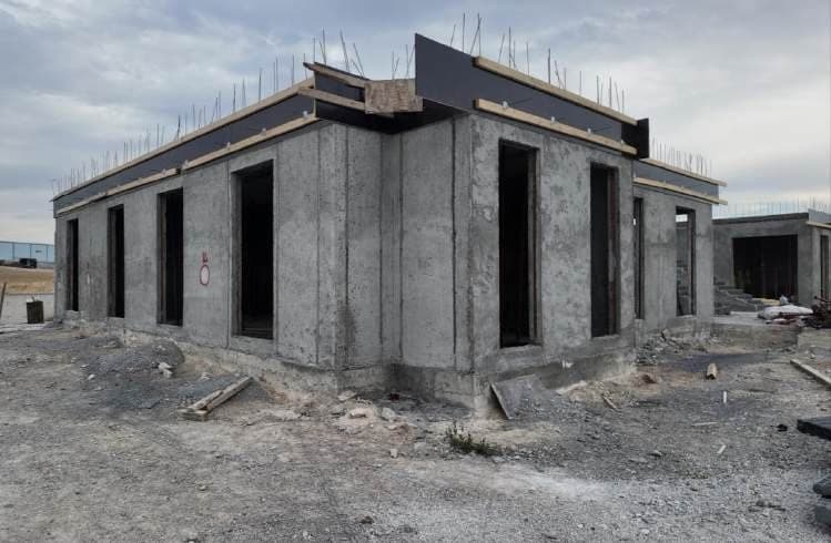 Single-storey rough structure with finished shotcrete walls, open door and window openings and reinforcement bars showing at the top.